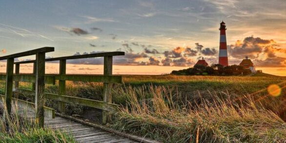 Sonnenuntergang mit Leuchtturm und Holzbrücke auf einer Wiese.