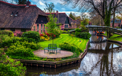 Malersiche Häuser am Kanal mit Brücke und üppigem Garten im Vordergrund.