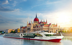 Kreuzfahrtschiff nickoVISION auf einem Fluss vor einem historischen Gebäude bei Sonnenuntergang.