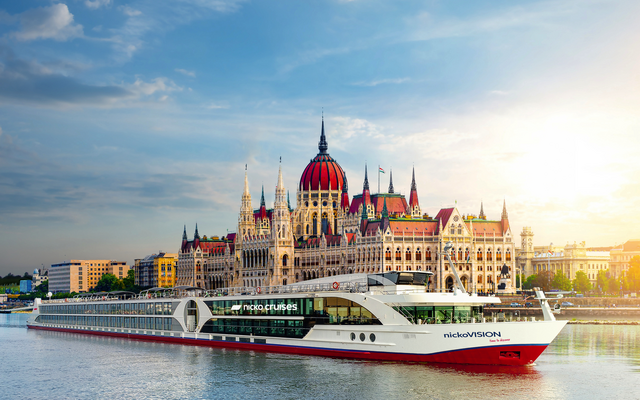 Kreuzfahrtschiff nickoVISION auf einem Fluss vor einem historischen Gebäude bei Sonnenuntergang.