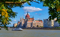 Parlamentsgebäude von Budapest, Ungarn, am Ufer der Donau, umrahmt von Bäumen im Vordergrund.