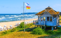 Strand mit Strandkörben, Haus am Meer und wehenden Flaggen.