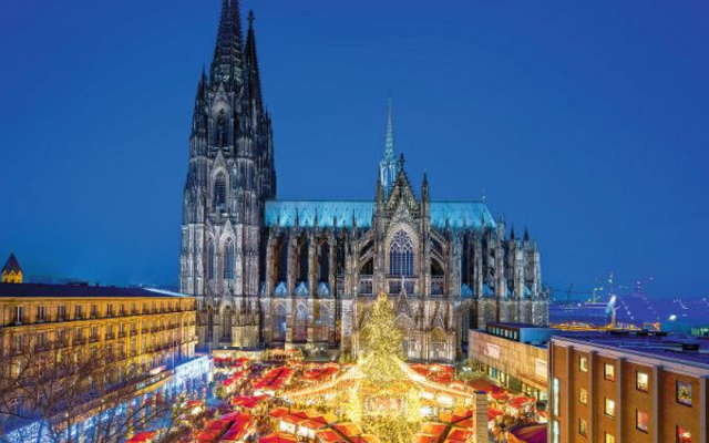 Kölner Dom bei Nacht mit beleuchtetem Weihnachtsmarkt im Vordergrund.