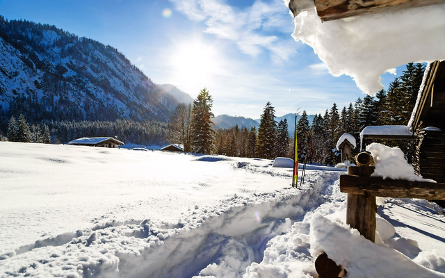 Winterlandschaft in Ruhpolding mit Sonne, verschneiten Bergen und Hütten.