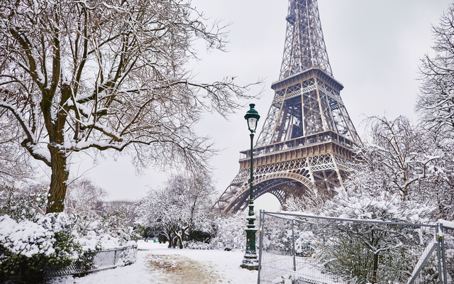 Eiffelturm im Winter mit Schnee bedeckt, Bäume im Vordergrund.