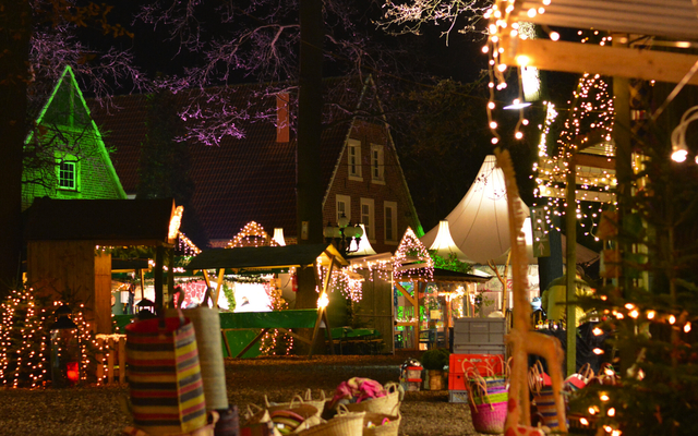 Weihnachtsmarkt mit Lichtern, Buden und beleuchteten Bäumen in Velen bei Nacht.