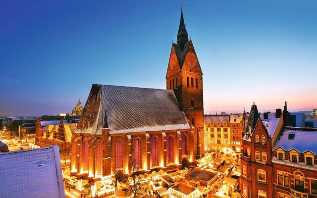 Kirche und beleuchteter Weihnachtsmarkt im Winter bei Dämmerung.