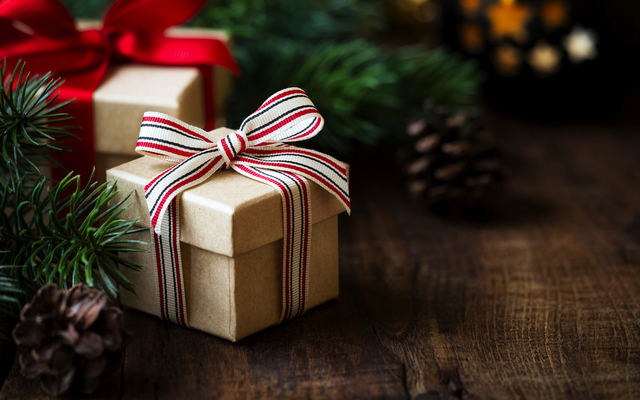 Geschenkboxen mit Schleifen auf Holztisch, umgeben von Tannenzweigen und Zapfen.