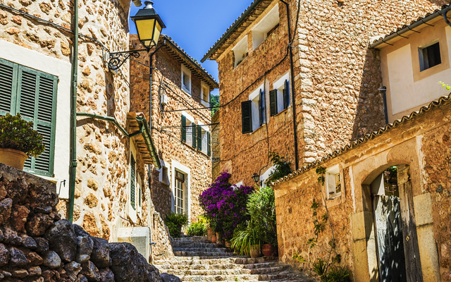 Kopfsteinpflasterstraße in einem mediterranen Dorf mit blühenden Pflanzen.