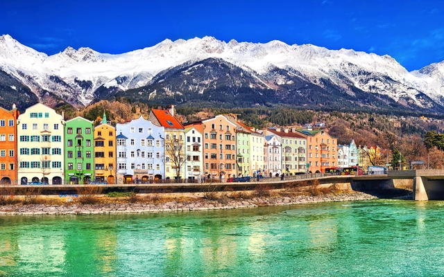 Bunte Häuser am Fluss vor schneebedeckten Bergen.