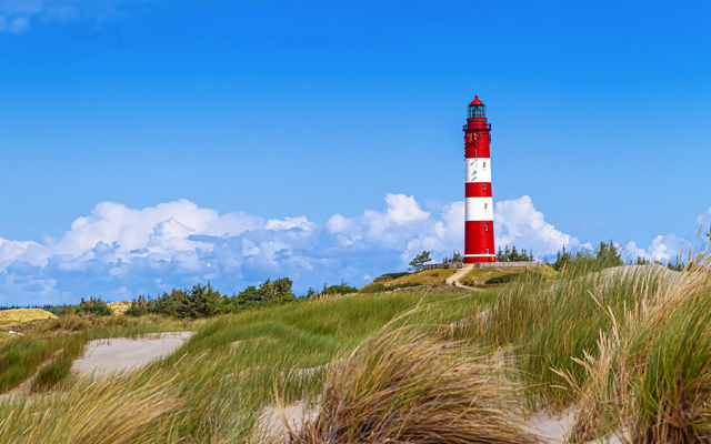 Leuchtturm in Dünenlandschaft unter blauem Himmel.