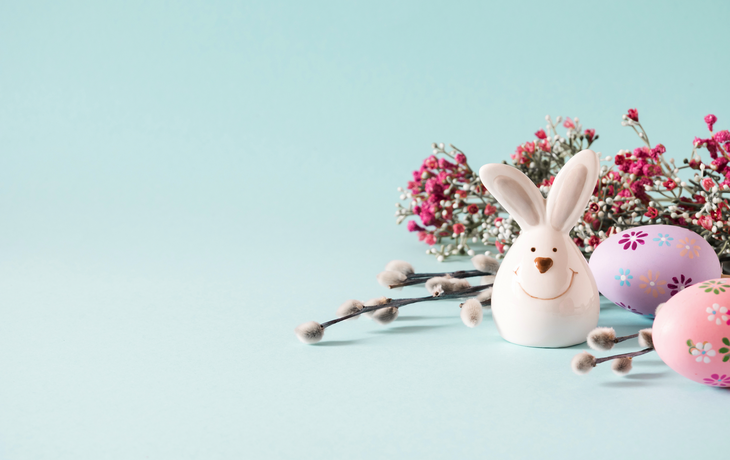Osterhase auf pastellblauem Hintergrund und Blumen. Minimalistisches Osterferienkonzept. 