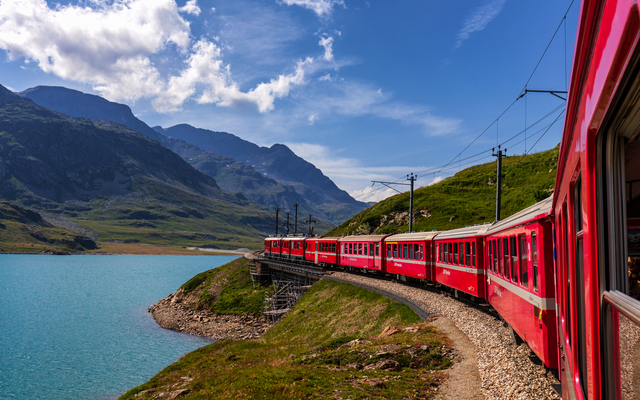 Roter Zug fährt am Seeufer in alpiner Landschaft entlang