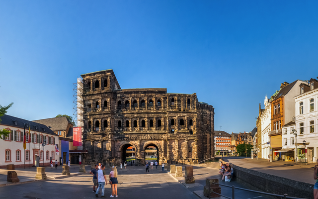 Menschen spazieren vor der Porta Nigra in Trier bei klarem Himmel.
