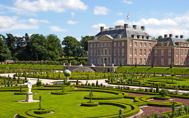 Herrenhaus mit gepflegtem Garten im Vordergrund bei sonnigem Wetter.