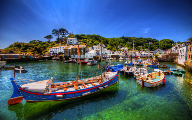Boote in einem malerischen Hafen mit klarem Wasser und Häusern im Hintergrund.