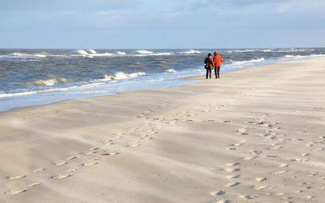 Zwei Menschen laufen am leeren Strand entlang, Meer im Hintergrund.