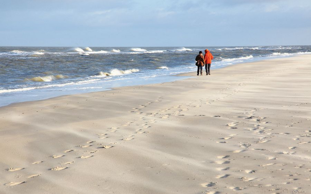 Zwei Menschen laufen am leeren Strand entlang, Meer im Hintergrund.
