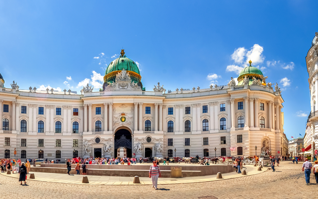 Panorama der Wiener Hofburg mit belebtem Platz und klarer Himmel im Hintergrund.