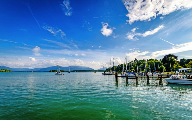 Boote an einem Steg in einem ruhigen See mit Bergen und blauem Himmel im Hintergrund.