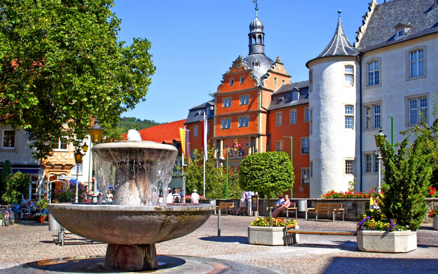 Historischer Platz mit Brunnen und farbigen Gebäuden im Hintergrund.