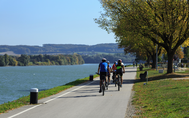 Radfahrer auf einem Weg entlang eines Flusses bei sonnigem Wetter.