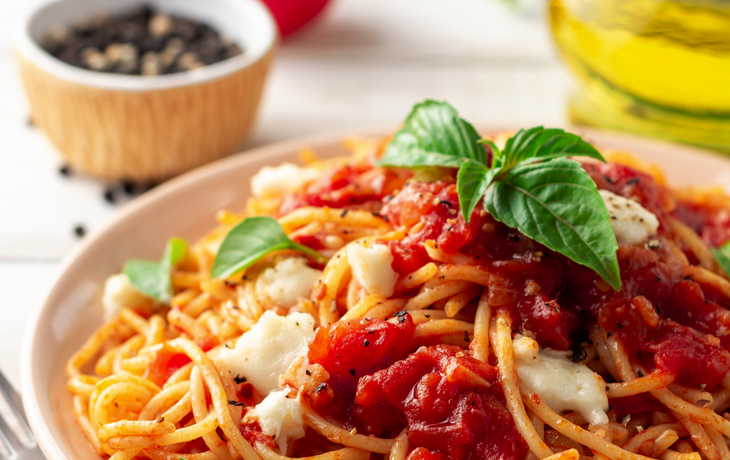 Spaghetti Nudeln mit Tomatensauce,Mozzarellakäse und frischer Basilikum in der Platte auf weißem hölzernem Hintergrund. Tiefenschärfe.