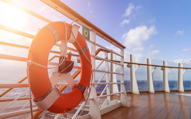 Rettungsring an der Reling eines Schiffsdecks mit Meereshintergrund bei sonnigem Wetter.