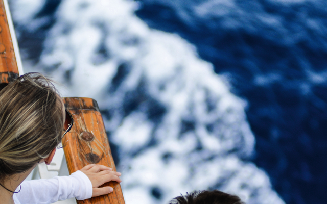 Junges Paar steht auf einem Kreuzfahrtschiffdeck und blickt aufs Meer.