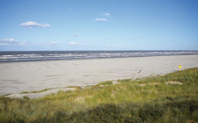 Ein sandiger Strand mit Dünen im Vordergrund und blauem Himmel im Hintergrund auf der Insel Juist.