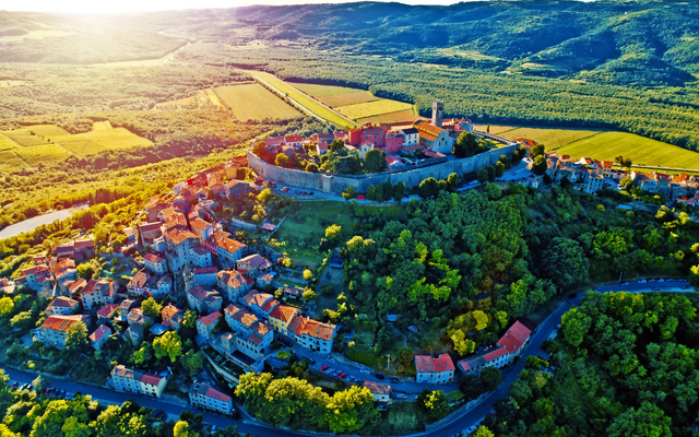 Luftbild einer malerischen Stadt auf einem Hügel mit umliegenden Wäldern und Feldern.