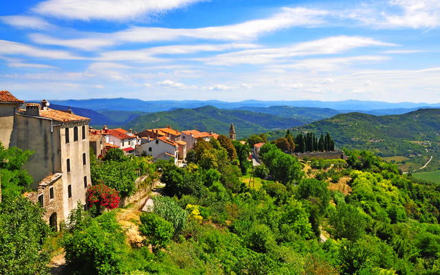 Blick auf ein malerisches Dorf in hügeliger Landschaft unter blauem Himmel.