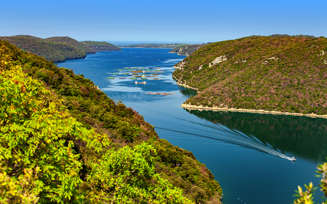 Flusslandschaft mit Hügeln und einem Boot auf dem Wasser bei klarem Himmel.
