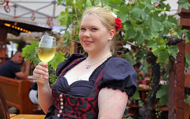 Frau in traditioneller Tracht mit Weinglas im Freien.