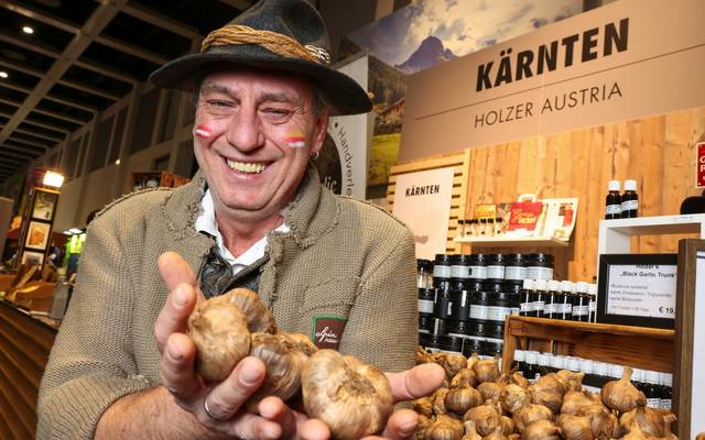 Ein Mann in Tracht hält Knoblauch vor einem Kärnten-Stand auf einer Messe.