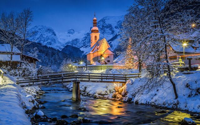 Verschneite Kapelle bei Abenddämmerung, Fluss und Berge im Hintergrund.