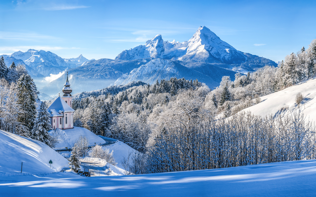 Verschneite Alpenlandschaft mit Kirche und Bergen im Hintergrund.