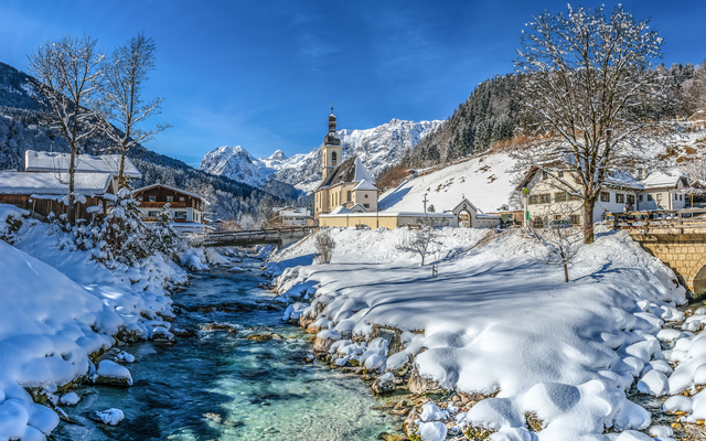 Verschneites Dorf mit Kirche und Bach im Winter.