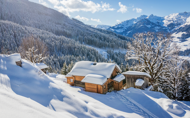 Verschneite Holzhütten in bergiger Winterlandschaft bei klarem Himmel.