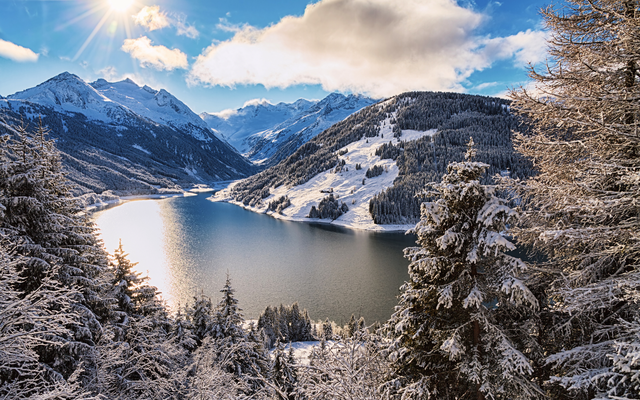 Verschneite Berge und See unter sonnigem Himmel im Winter.
