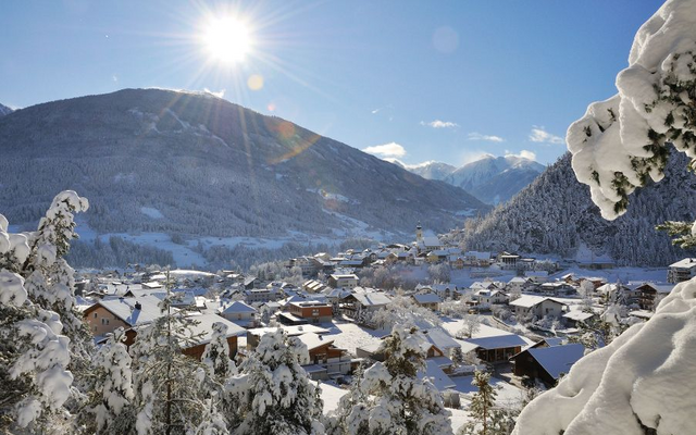 Verschneites Dorf im Pitztal mit Bergen und Sonne im Hintergrund.