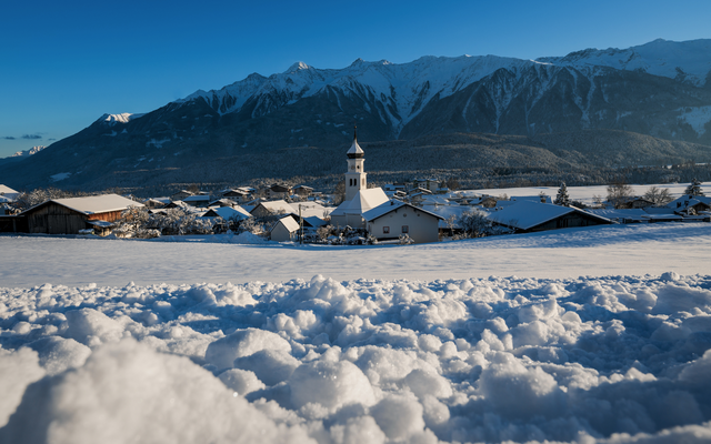 Verschneite Landschaft mit Dorf und Kirche vor Bergkulisse.