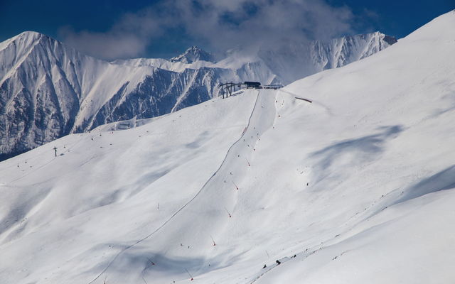 Skipiste im Hochgebirge mit Seilbahn und schneebedeckten Bergen im Hintergrund.