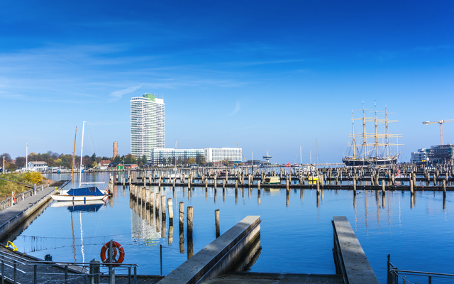 Yachthafen mit Schiffen und Hochhaus im Hintergrund an einem klaren Tag.