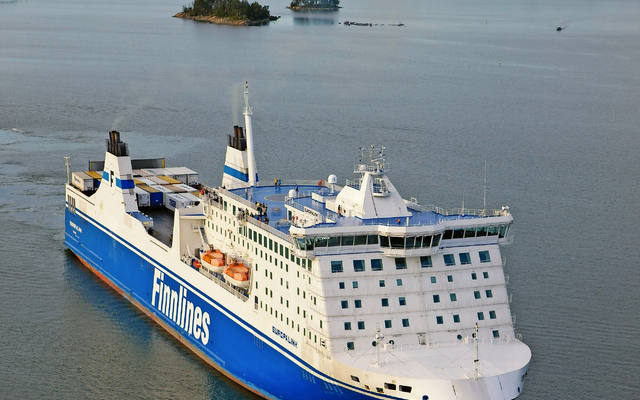 Ein großes Fährschiff auf offenem Wasser mit bewaldeter Küste im Hintergrund.