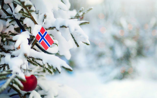 Verschneiter Weihnachtsbaum mit norwegischer Flagge und roten Kugeln.
