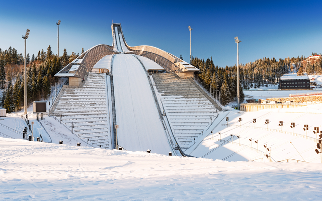 Skisprungschanze im Winter mit verschneiter Landschaft und blauem Himmel.