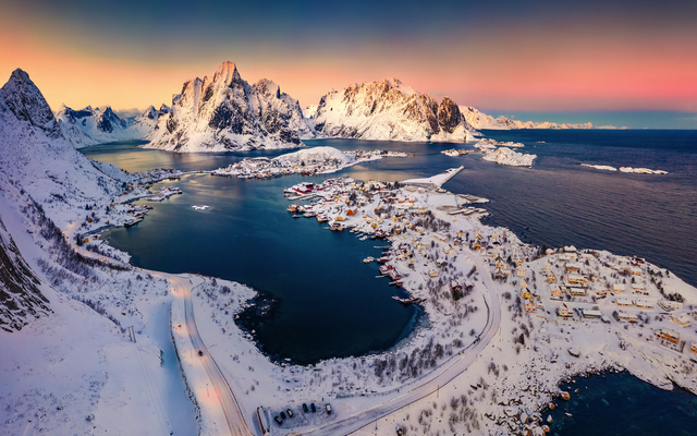 Winterliche Landschaft mit verschneiten Bergen und einem fjordähnlichen See bei Sonnenuntergang.