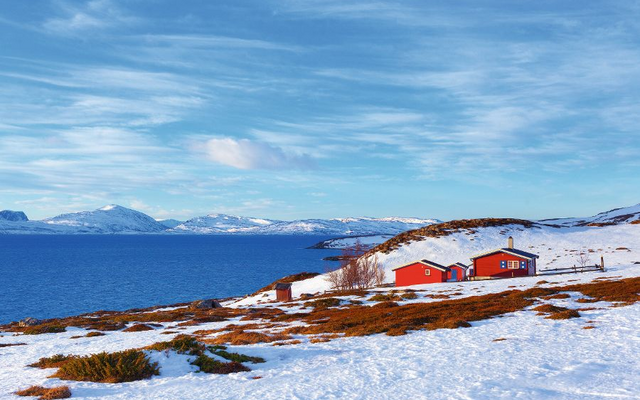 Winterliche norwegische Landschaft mit einem Fjord und einem roten Holzhaus im Vordergrund.