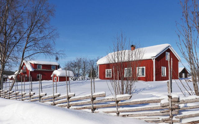 Rote Holzhäuser im Schnee mit Holzzaun und blauem Himmel.